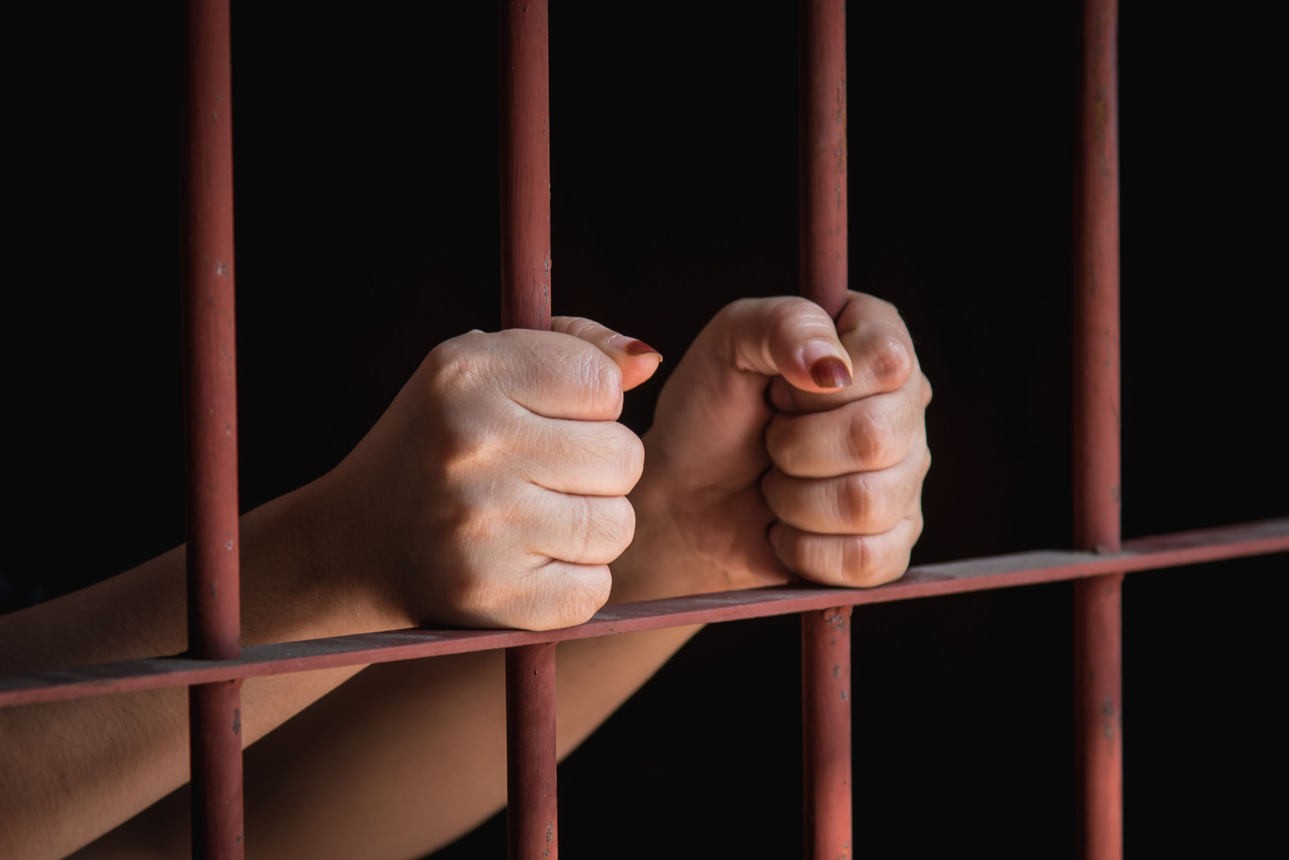 hands of woman holding bars in jail