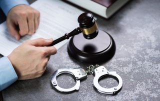 Close-up Of A Judge Hand Striking Gavel With Handcuffs On Desk In Courtroom